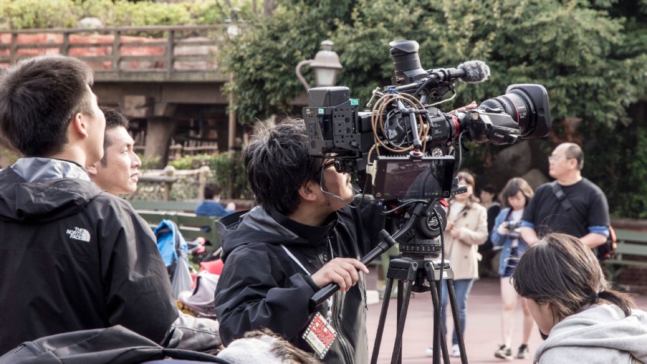 FILM CREWパスを付けた撮影クルーがプロ用カメラで屋外撮影する様子